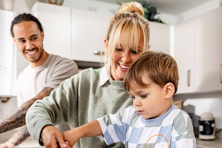 Mum helping her son pour milk into a mug in the kitchen