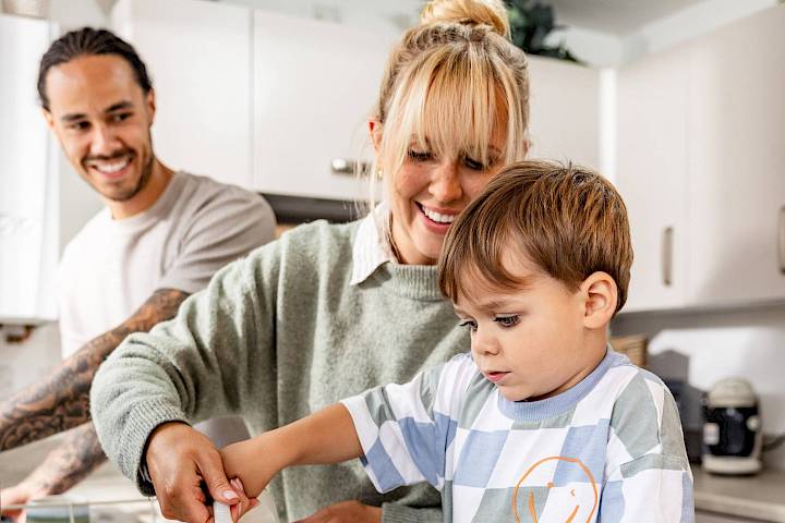 Mum helping her son pour milk into a mug in the kitchen