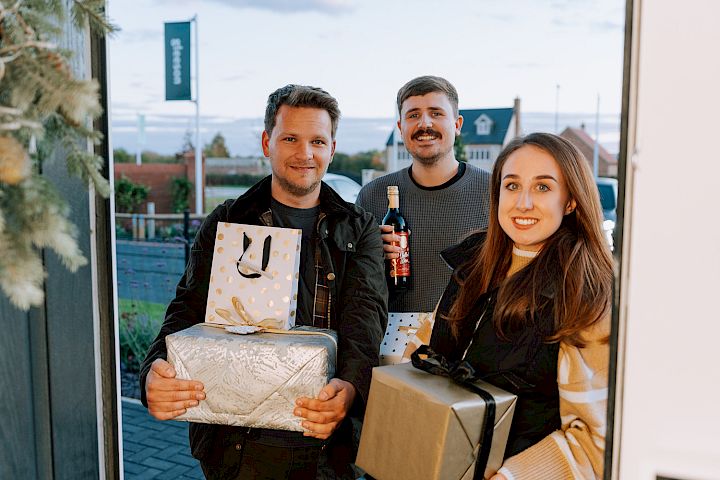 Young adults standing outside a front door with Christmas gifts